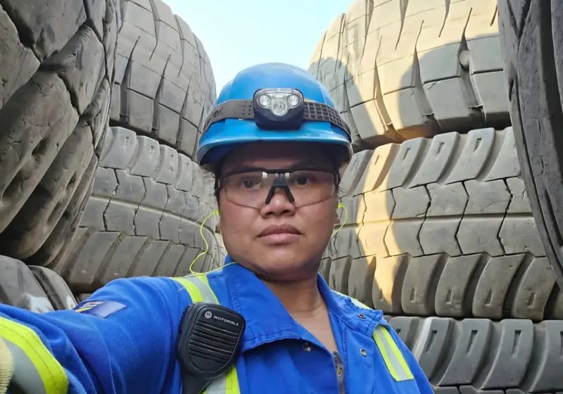 Woman in a blue hard hat, safety glasses and hi-vis coveralls standing among giant mining truck tires